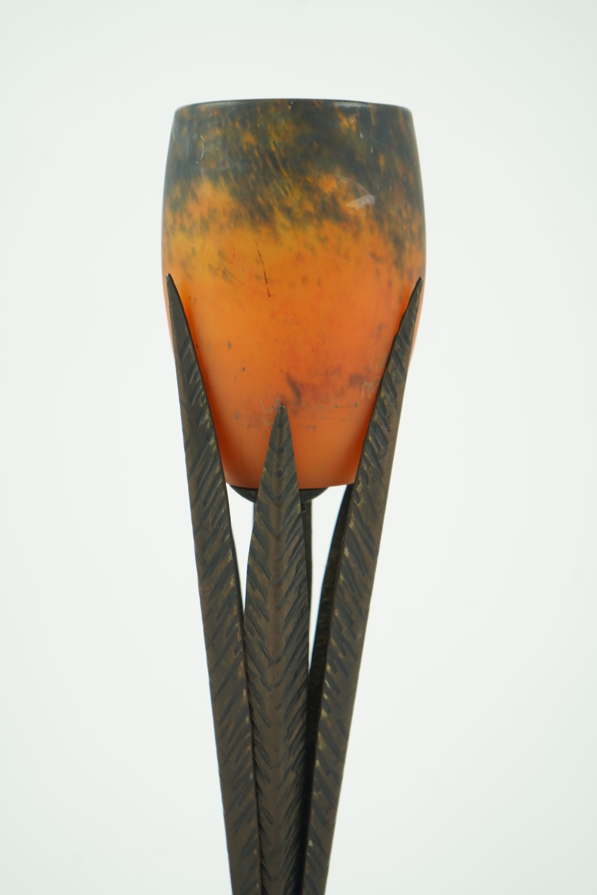 Manner of Muller Freres and Robj: A French Art Deco table lamp the mottled orange glass shade supported by naturalistic palm-leaf metal supports terminating in a circular hammered metal base, 40cm high